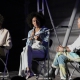 Helga Davis, Naima Ramos-Chapman, and Dawn Lundy Martin sit onstage. Naima speaks into a handheld mic.